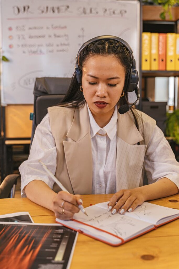 Woman Wearing a Headset Writing in a Notebook 